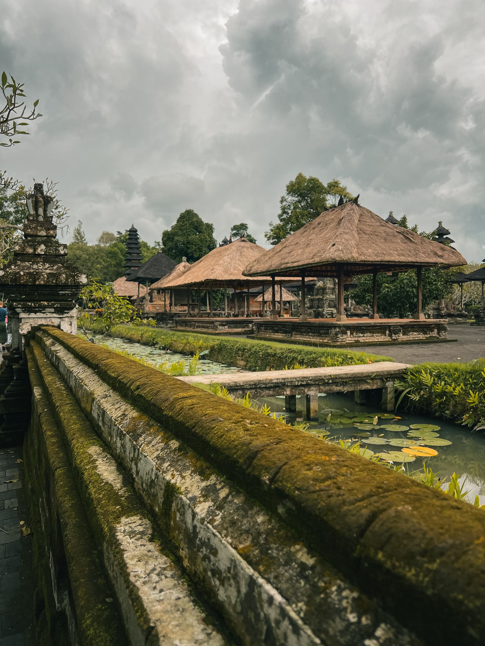 A quiet Balinese temple garden with thatched pavilions and a lily pond